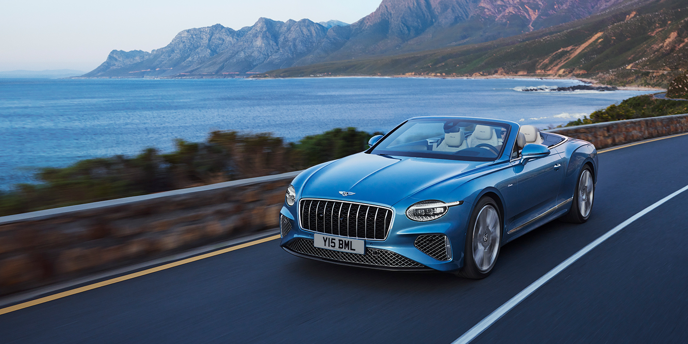 Bentley Valencia New Bentley Continental GTC Azure convertible in Light Windsor blue paint with 22 inch Azure wheels and chrome grill, driving dynamically by the sea