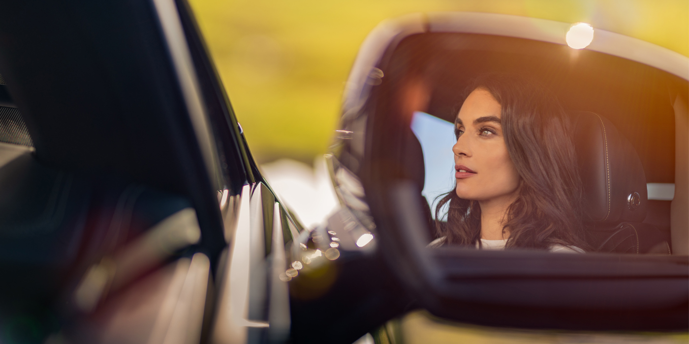 Bentley Valencia profile of dark haired woman's face in mirror of Bentley car in sunlight