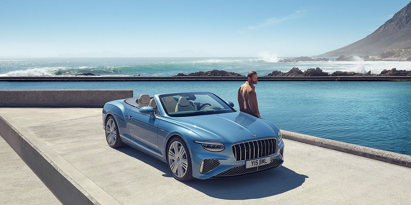 Bentley Valencia New Bentley Continental GTC Azure convertible front view in Light Windsor blue paint with 22 inch ten spoke wheels parked by the sea in the sunshine