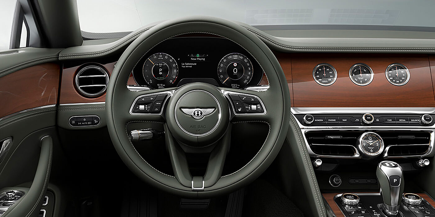 Bentley Valencia New Bentley Flying Spur sedan front cabin in Cumbrian Green hide and Crown Cut walnut veneer showing steering wheel and Rotating Display with three clocks on face