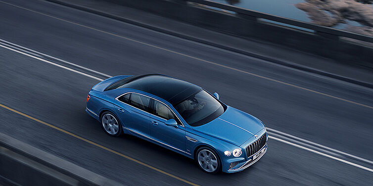 Bentley Valencia New Bentley Flying Spur Azure sedan in Light windsor blue paint by Mulliner, with 22 inch Azure wheels seen from overhead driving dynamically on a country road