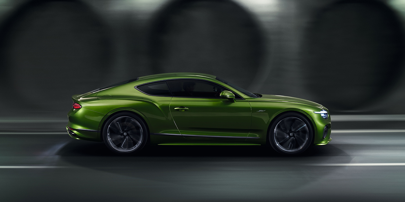Bentley Valencia Bentley Continental GT coupe in Tourmaline Green paint driving in profile on a dark road