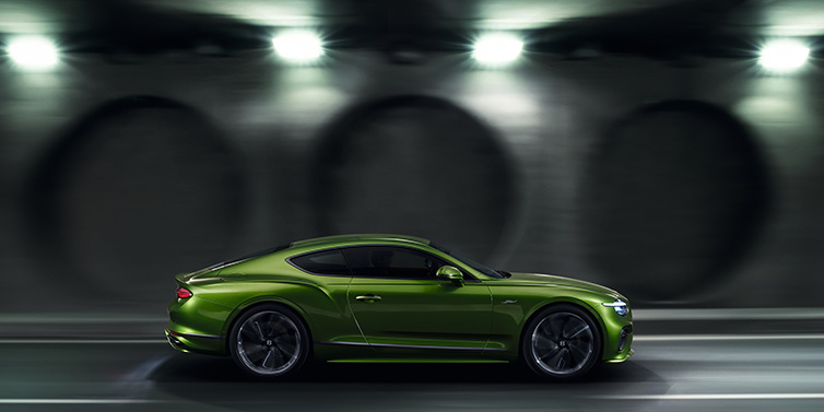 Bentley Valencia Bentley Continental GT Speed coupe profile in Tourmaline Green drivig dynamically past a concrete wall at night