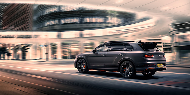 Bentley Valencia Bentley Bentayga S Black Edition SUV rear thre quarter in Anthracite Satin paint driving dynamically through a city at night