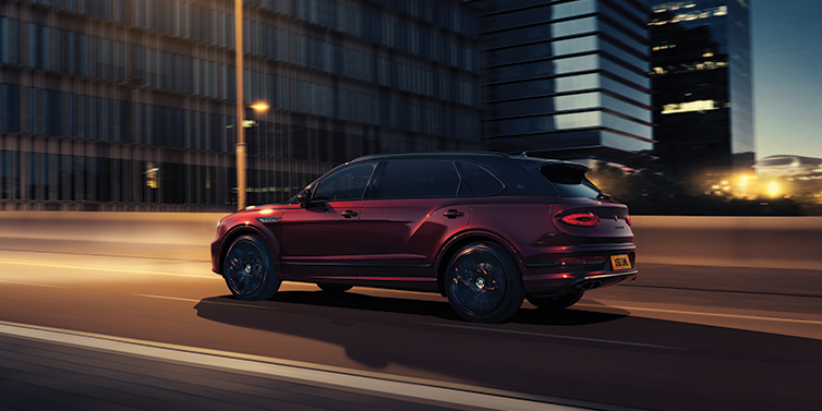 Bentley Valencia Bentley Bentayga Extended Wheelbase Mulliner SUV in Cricket Ball red paint driving dynamically in city at night