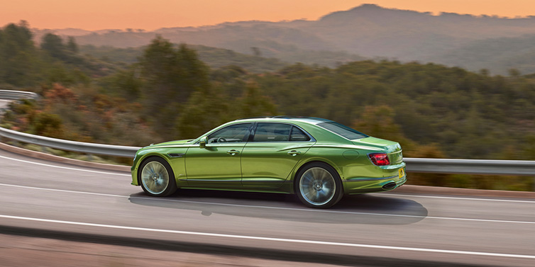 Bentley Valencia Bentley Flying Spur Speed sedan side profile in Tourmaline Green paint driving dynamically on a mountain road at sunset