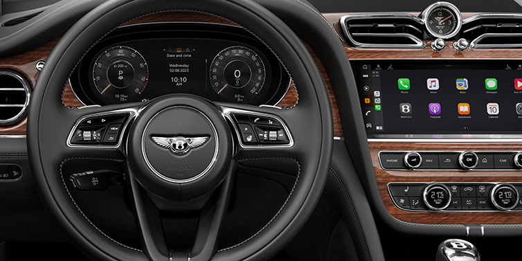 Bentley Valencia Bentley Bentayga SUV front interior detail of steering wheel and driver screens surrounded by Beluga black hide and Crown Cut Walnut veneer