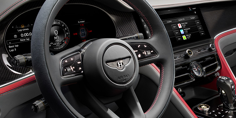 Bentley Valencia Bentley Flying Spur Speed sedan front interior detail showing steering wheel and driver screens surrounded with Hotspur red and Gravity Grey hides